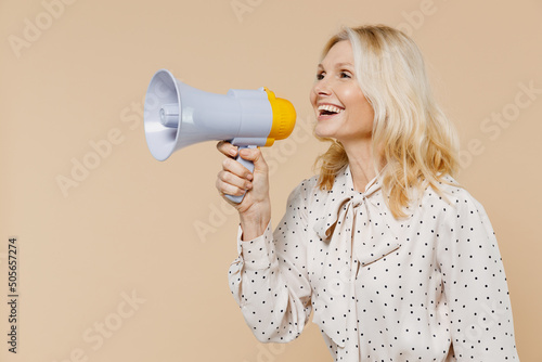 Excited happy elderly gray-haired blonde woman lady 40s years old wears pink dress hold scream in megaphone announces discounts sale Hurry up isolated on plain pastel beige background studio portrait.