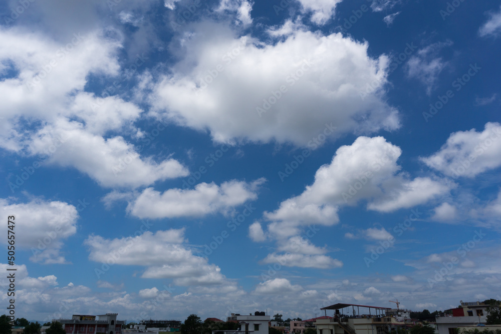 25th july 2020. dehradun,uttarakhand, India. Different shapes of white clouds forming on the blue skies with residential housing and buildings. 25th july 2020. dehradun,uttarakhand, India. Different shapes of white clouds forming on the blue skies with residential housing and buildings.