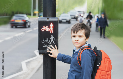 School kid pressing a button at traffic lights on pedestrian crossing on way to school. Child boy with backpack using traffic signal controlled pedestrian facilities for crossing road. photo