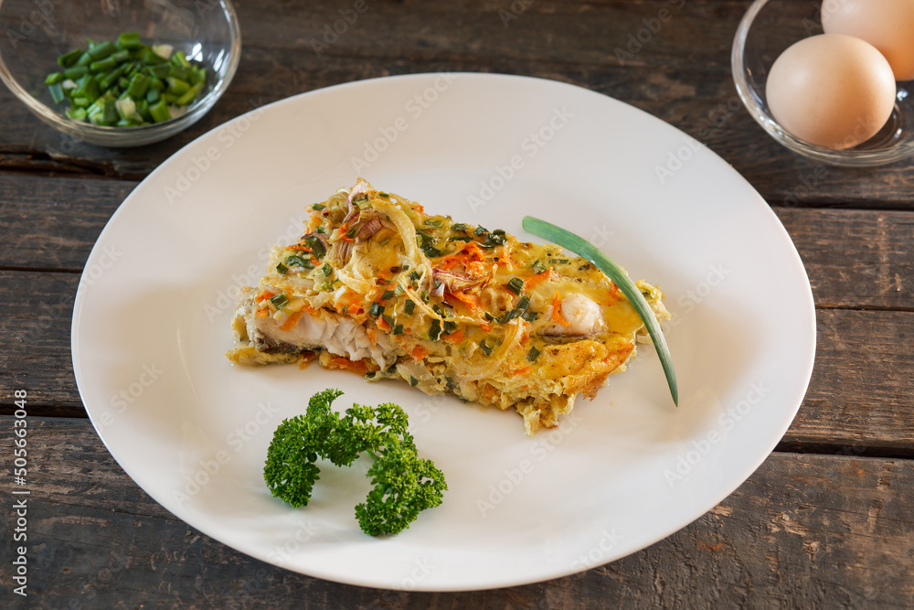 A piece of Pie made from fish, eggs, onions and carrots. White plate, wooden planks A piece of Pie made from fish, eggs, onions and carrots. White plate, wooden planks