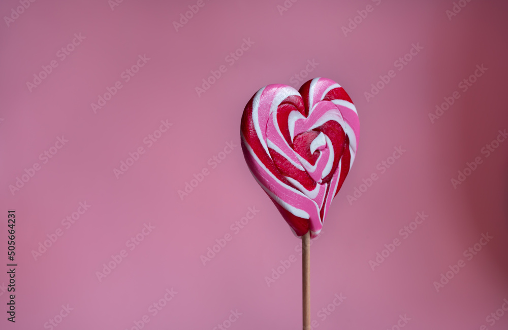 Vertical photo of  festive sweets for  beloved  Pink  background. Sweet heart shaped candy on stick. Romantic valentine day food. Heart shaped lollipop close up.