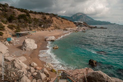 The sandy shore of the Black Sea with stone boulders. Surf with turquoise water