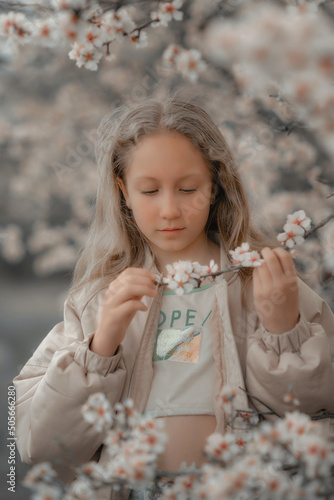 A girl in a blooming almond orchard, holding a twig in her hands