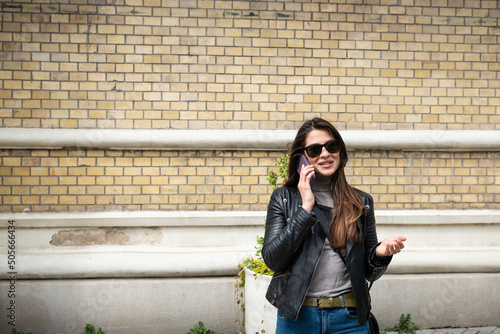 Young business woman talking on smartphone outdoor. Attractive girl in leather jacket having conversation with her friends waiting for the to go on the rock music concert. © Srdjan