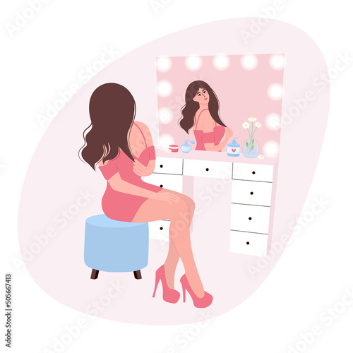 Young pretty woman sitting in front of a dressing table and admiring herself. Makeup, beauty care routine