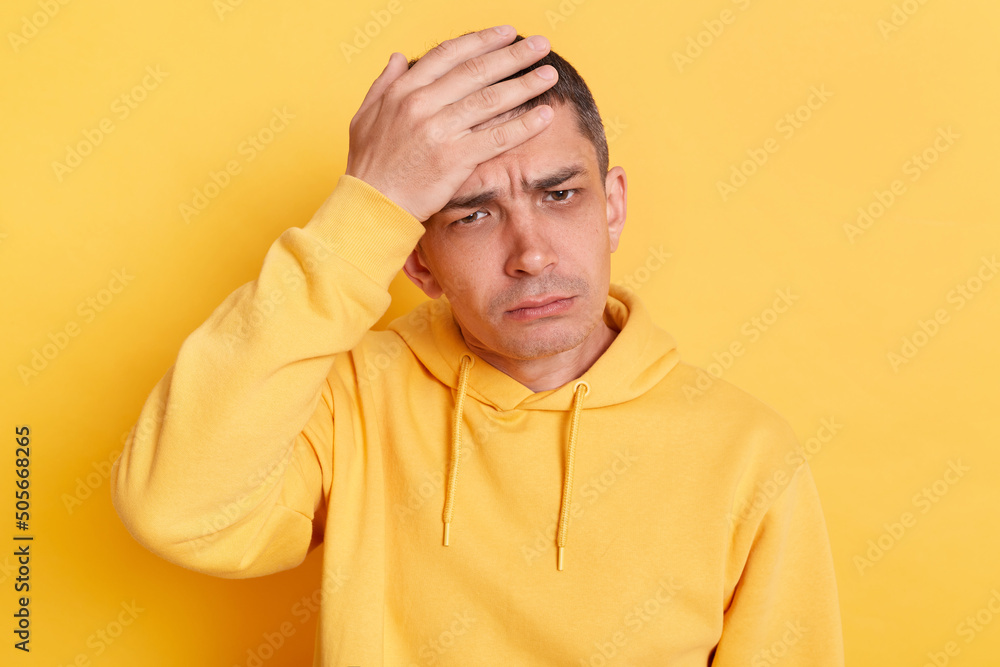 Unhappy sad man wearing casual style hoodie, posing isolated over yellow background, making facepalm gesture, loser, forget about something important. Unhappy sad man wearing casual style hoodie, posing isolated over yellow background, making facepalm gesture, loser, forget about something important.