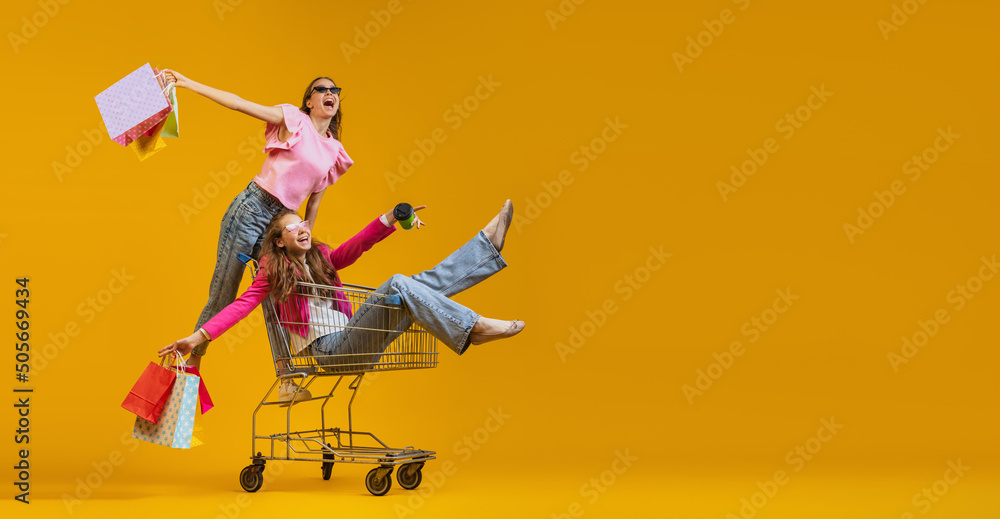 Ταπετσαρία Two young excited girls go shopping with shopping cart isolated on bright yellow background