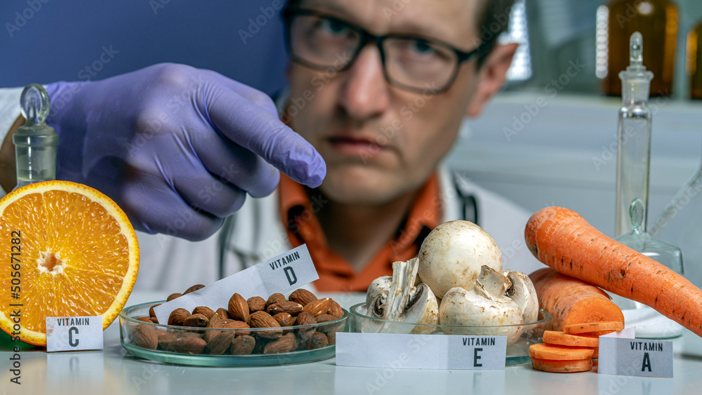 Oranges, mushrooms, nuts and carrots on a laboratory table with the names of vitamins. Essential vitamins. Doctor in Food test laboratory.