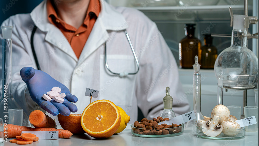 Pills and Oranges, mushrooms and nuts on a laboratory table with vitamin names.The doctor is holding pills. Essential vitamins in Food laboratory. Pills and Oranges, mushrooms and nuts on a laboratory table with vitamin names.The doctor is holding pills. Essential vitamins in Food laboratory.