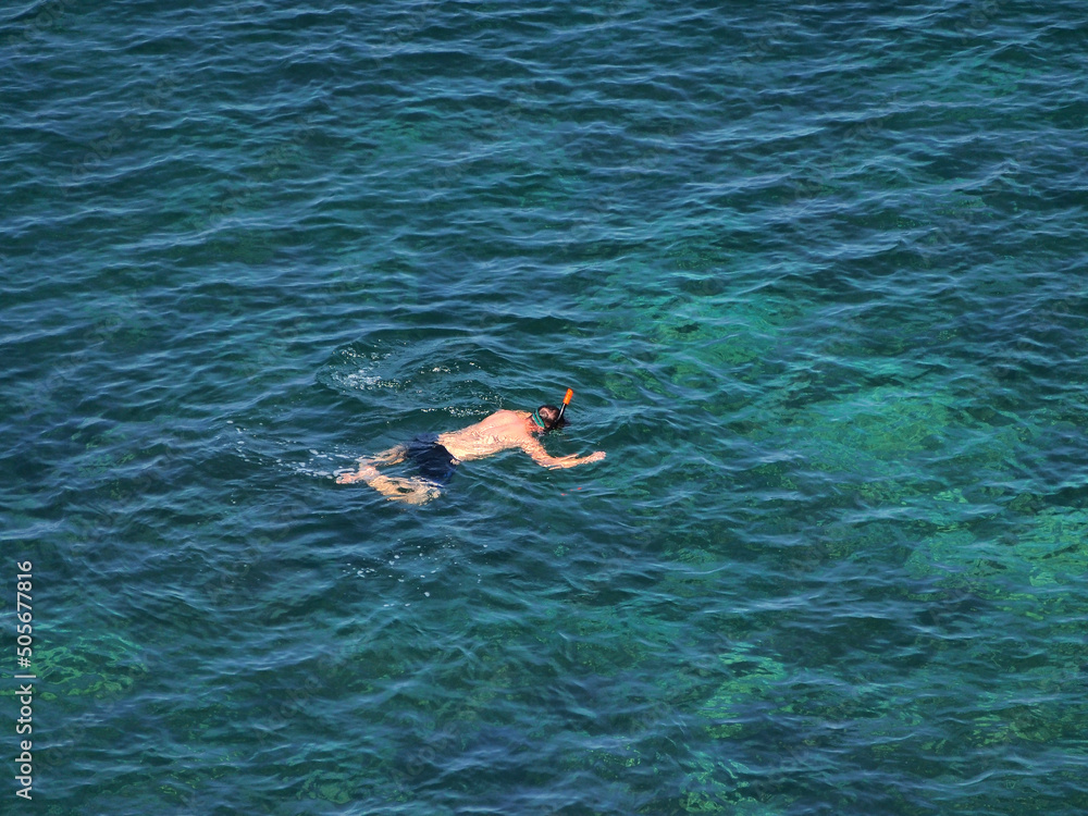 A free diver swimming in a blue, transparent sea.