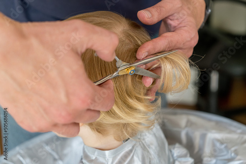 hands doing toddler haircut with hairdresser scissors with thinning layering blade at home. Baby boy hair cut diy