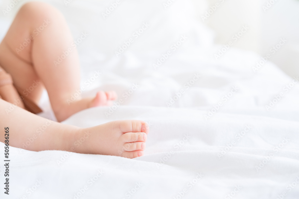 Close up baby barefooted legs feet lying on white bed linen. Neutral pastel light color tones