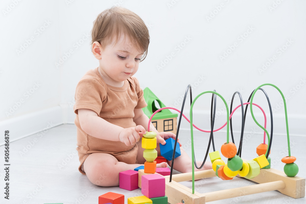 cute baby girl in brown bodysuit playing with colorful wooden toys on white room cute baby girl in brown bodysuit playing with colorful wooden toys on white room