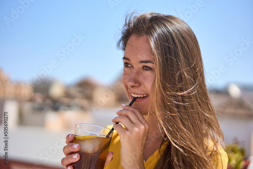 young happy woman having a could drink on the terrace of a Spanish café wearing a yellow blouse on a hot summer day