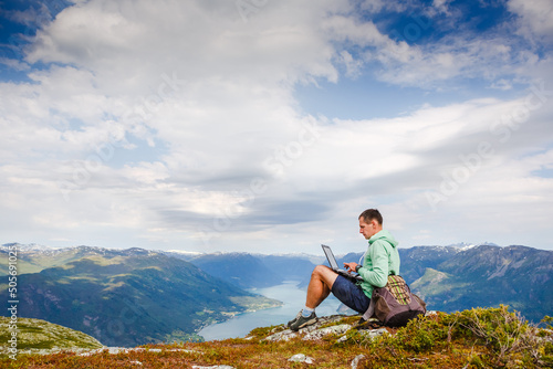 Young man sitting on the cliff using laptop