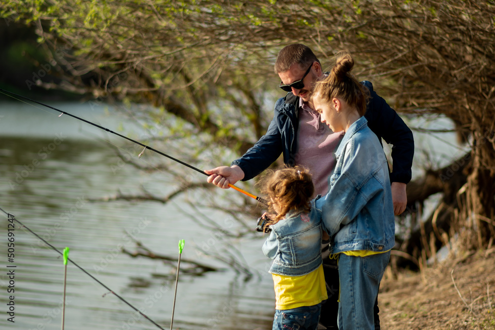 A dad and his two daughters are fishing in the river. It's early spring outside. Family vacation. Hobby. Time with family. Together. Lifestile. A dad and his two daughters are fishing in the river. It's early spring outside. Family vacation. Hobby. Time with family. Together. Lifestile.