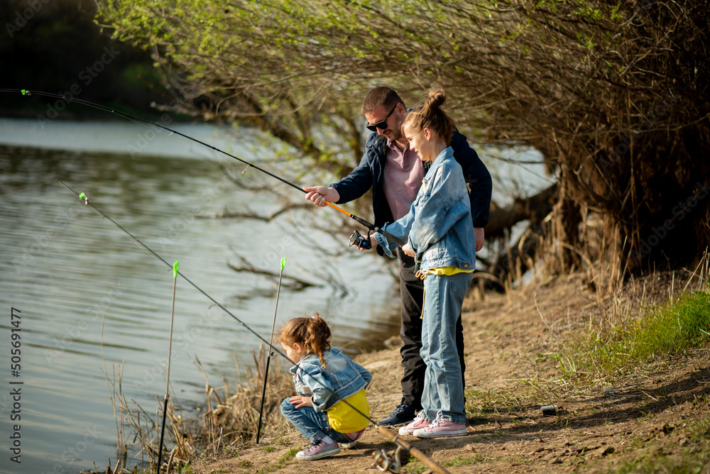 A dad and his two daughters are fishing in the river. It's early spring outside. Family vacation. Hobby. Time with family. Together. Lifestile. A dad and his two daughters are fishing in the river. It's early spring outside. Family vacation. Hobby. Time with family. Together. Lifestile.