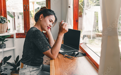 Beautiful Asian woman sits down at the bar counter in a coffee shop with a cup of coffee and smiles relaxingly after she's done working online on her laptop.. photo