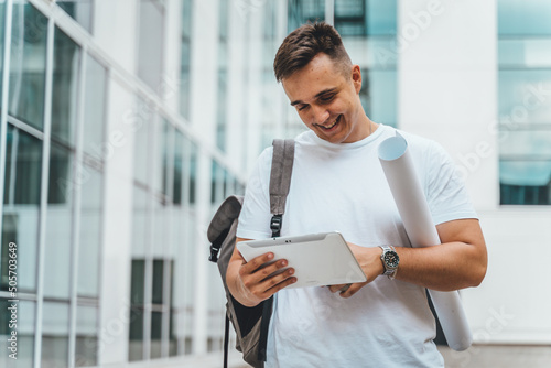 A young student in front of his faculty building searching in his backpack, using phone and tablet and drinking coffee during the day © Dusan