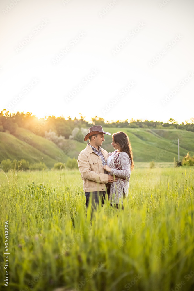 young beautiful couple, standing on a green meadow in the rays of the setting sun, cowboy clothes.rustic style young beautiful couple, standing on a green meadow in the rays of the setting sun, cowboy clothes.rustic style