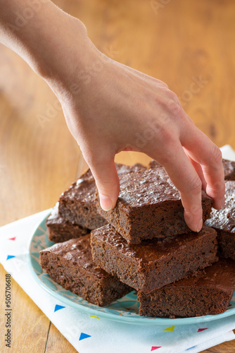 Woman's Hand Reaching for Homemade Baked Chocolate Brownies on a Plate with Copy Space in Background