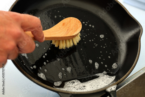 Foto Close up A hand holding bamboo cleaning brush scrub and washing the dirty cast iron pan with a pattern of grease and oil stains