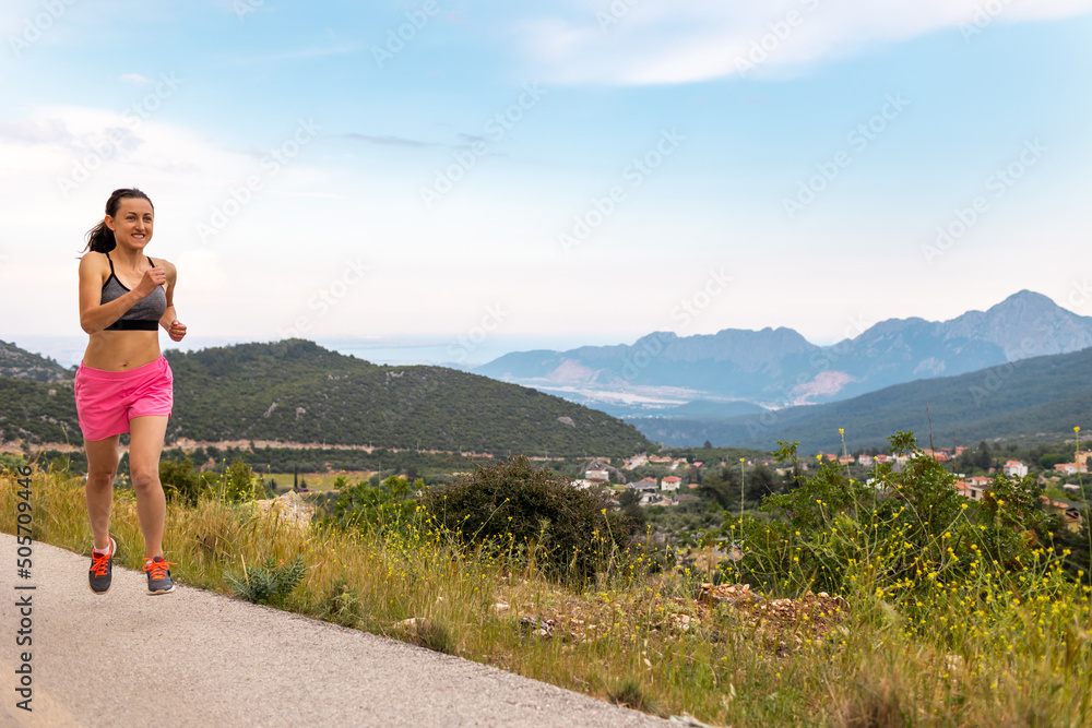 A girl runs along an asphalt road against the backdrop of beautiful mountains