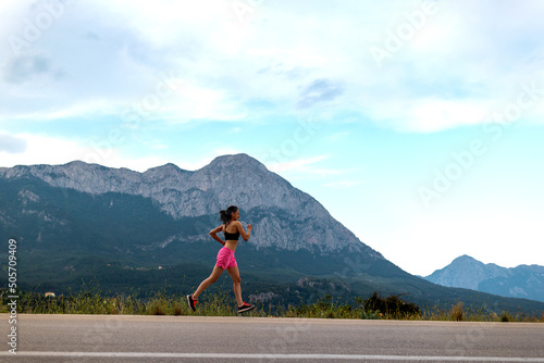 A girl runs along an asphalt road against the backdrop of beautiful mountains