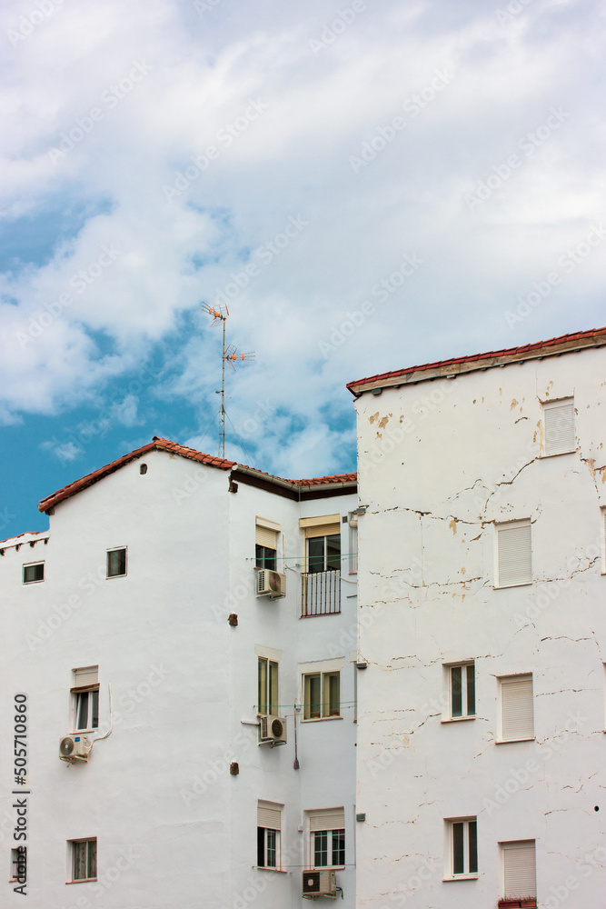 Front view of old residential white houses against blue sky in nice day. Beautiful postcard of a city from a trip. Vintage Spanish architecture. Historic Quarter in town of Portugal. Cracked facades.