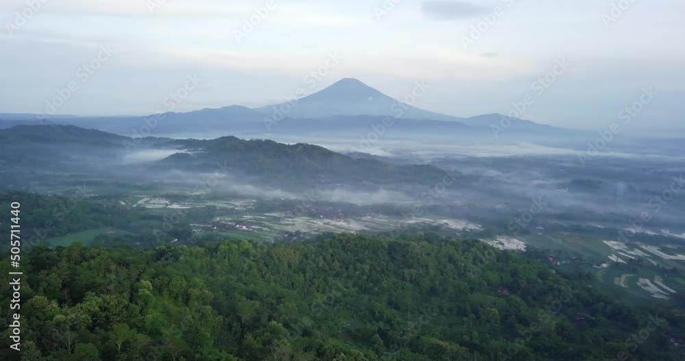Aerial view over green forest trees, clouds and fog in the valley and MOunt Sumbing in background
Aerial view over green forest trees, clouds and fog in the valley and MOunt Sumbing in background