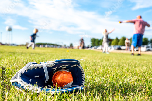 Youth sized glove with a baseball inside sitting on a grass field with players in the background