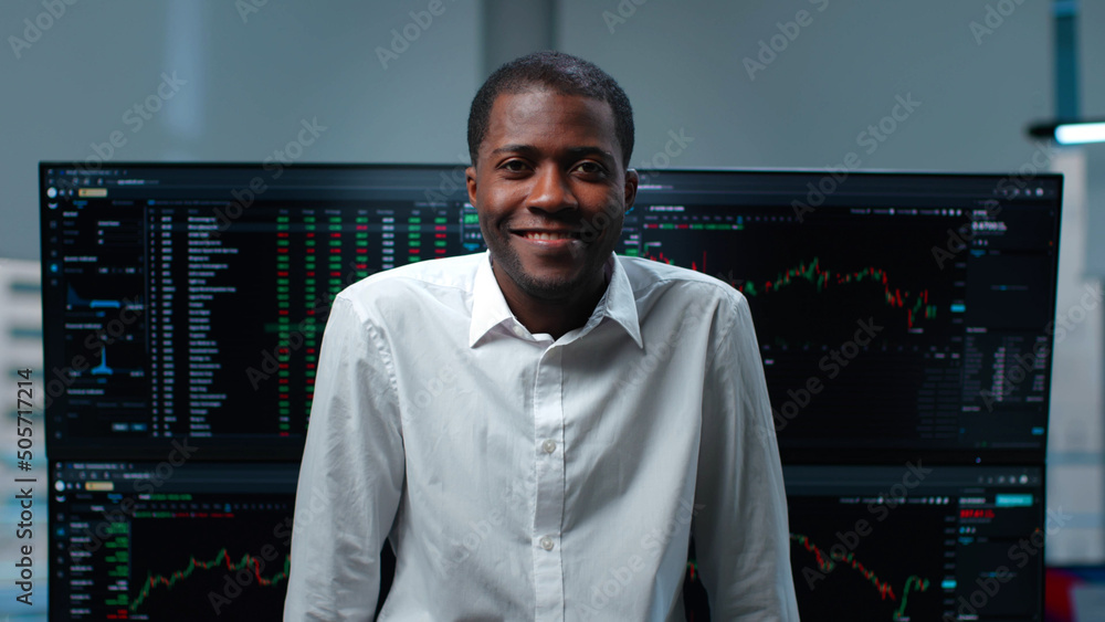 African-American man looking at camera with multiple computer monitors with p data on screens  - obrazy, fototapety, plakaty 