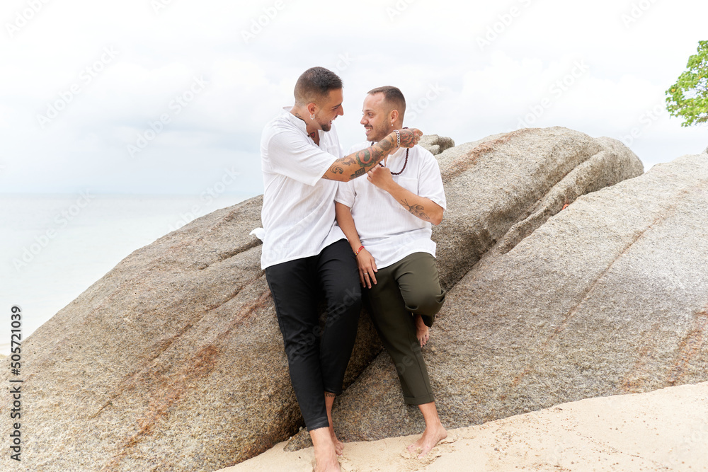 Homosexual man giving a ball necklace to his partner in a tropical beach Homosexual man giving a ball necklace to his partner in a tropical beach
