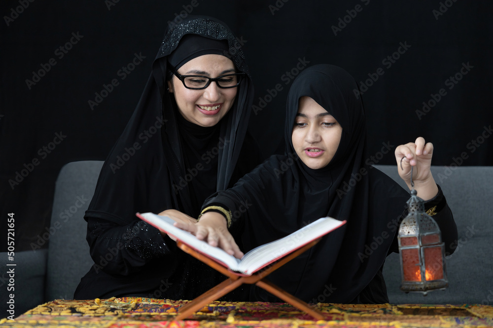 muslim mother with her daughter reading a holy book Quran and holding lamp on black background muslim mother with her daughter reading a holy book Quran and holding lamp on black background