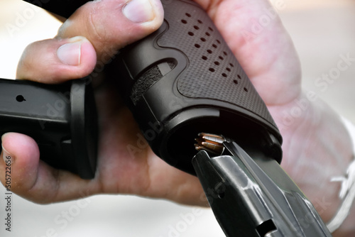 The shooter is using his hand to push the full magazine into the pistol grip to fill the barrel of the gun or reload new gun magazines. Soft and selective focus.