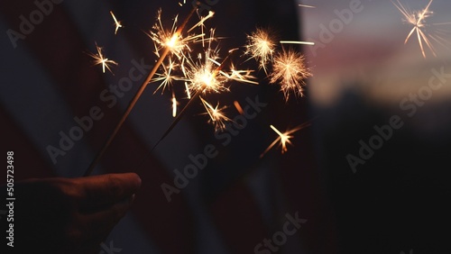 Happy 4th of July Independence Day, Hand holding Sparkler fireworks USA celebration with American flag background. Concept of Fourth of July, Independence Day, Fireworks, Sparkler, Memorial, Veterans