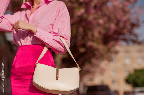 Trendy spring fashion outfit with white faux leather bag, handbag, pink shirt, satin skirt. Stylish details. Copy, empty space for text