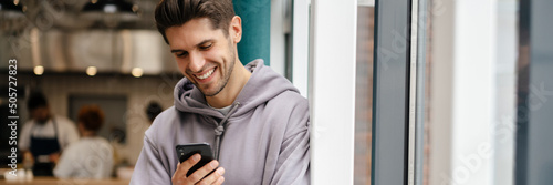 Happy young brunette man holding mobile phone