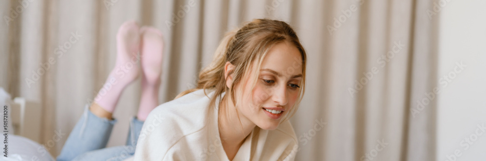 Young woman working with laptop and smiling in bedroom at home Young woman working with laptop and smiling in bedroom at home