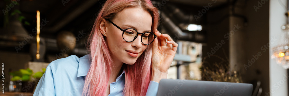 Young smiling woman working with laptop while sitting in cafe Young smiling woman working with laptop while sitting in cafe