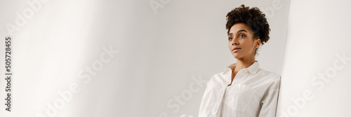 Young black woman leaning on wall and looking aside indoors