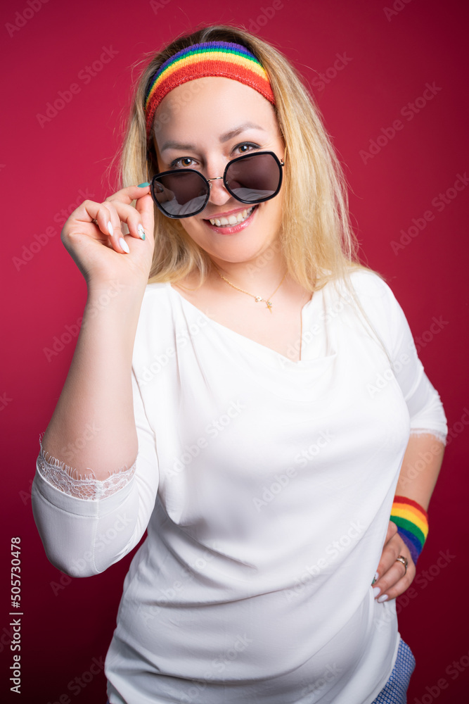 Joyful LGBT woman adjusting sunglasses ad smiling at camera against burgundy background Joyful LGBT woman adjusting sunglasses ad smiling at camera against burgundy background