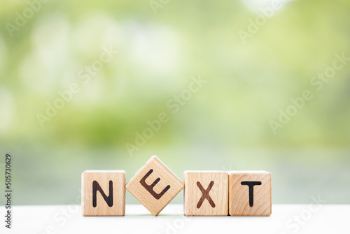 NEXT - word is written on wooden cubes on a green summer background. Close-up of wooden elements.