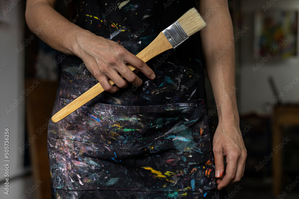 Obraz premium Close-up of the hands of an unrecognizable Latin American artist in apron showing a brush that she uses to paint in her art studio. Artist and hobby concept