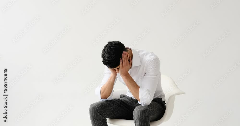 Depressed man feeling restless while sitting against white background Depressed man feeling restless while sitting against white background