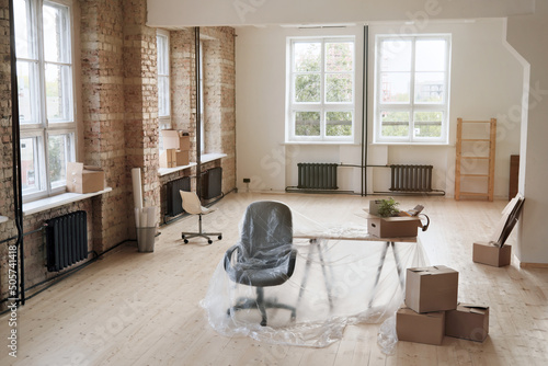 Interior of modern office space with brick wall and office furniture under polyethylene during renovation