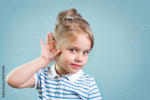 Child with hearing problem on blue background empty copy space. Hearing loss, symptoms and treatment concept. photo