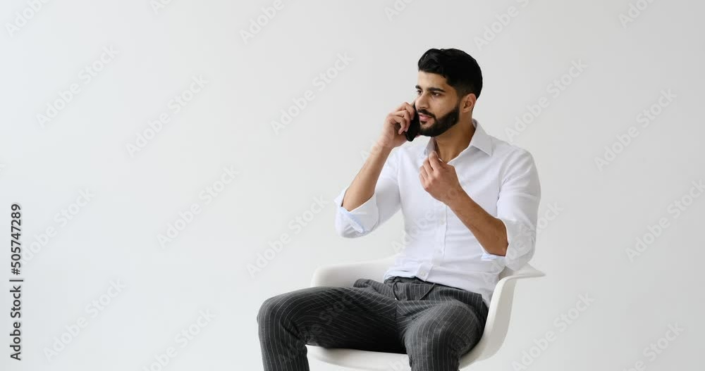 Angry man talking on mobile phone arguing or solving problem while sitting against white background Angry man talking on mobile phone arguing or solving problem while sitting against white background