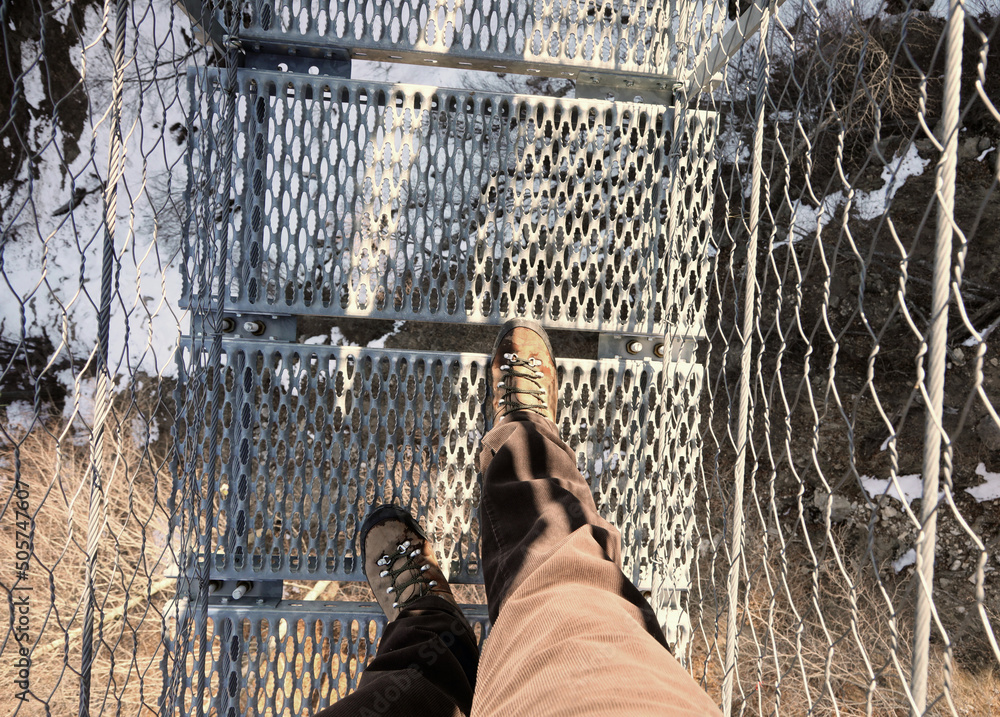 Φωτογραφία lightweight boots of man on the spectacular suspension bridge made of steel rope