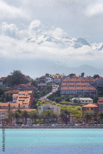 Fotografía vertical de una de las empinadas calles de San Vicente de la Barquera, con el mar azul al frente y los Picos de Europa tras las nubes, al fondo. photo